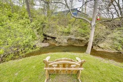 a wooden bench sitting in the grass next to a river at Serene Zanesville Getaway Hot Tub, 2 Decks! in Zanesville