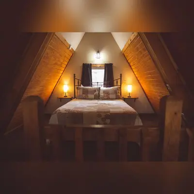 a small attic bedroom with a bed with two lamps at A-Frame #02 - by The Chalets in Logan