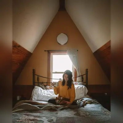 a woman sitting on a bed in a attic at A-Frame #15 - by The Chalets in Logan