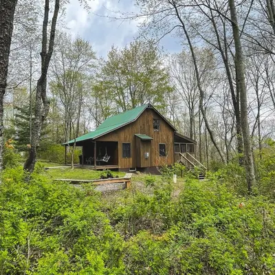 a wooden cabin with a green roof in the woods at Hawks Peak - by The Chalets in Logan