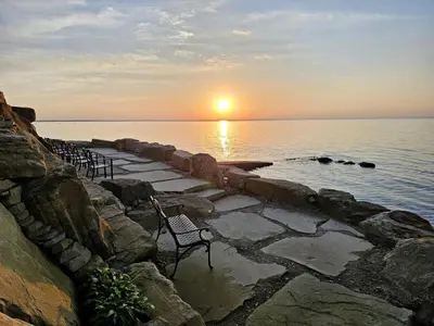 a row of chairs sitting on a stone path near the water at Rustic Lakeside Vacation Rental with Beach Access in Vermilion, Ohio in Vermilion