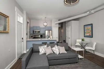 a living room with a gray couch and a kitchen at Heart of Mainstrasse 3 in Covington
