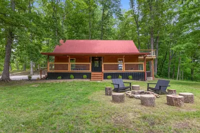 a log cabin in the woods with chairs and a fire pit at Hot Tub - Furnace Mountain Retreat - #RRG in Stanton