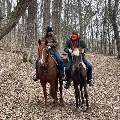 two people riding on horses in the woods at The Hampton - An Amish Built Deluxe Log Cabin in Genoa