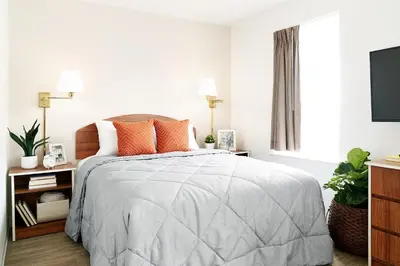 a white bedroom with a bed with orange pillows at InTown Suites Extended Stay Cincinnati OH - Colerain in Cincinnati