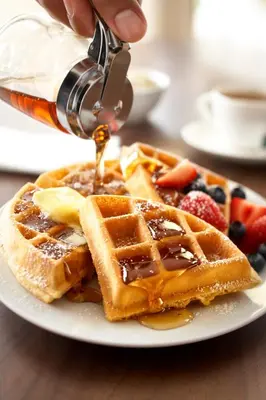 a person is pouring syrup onto a plate of waffles at Country Inn & Suites by Radisson, Columbus West, OH in Columbus